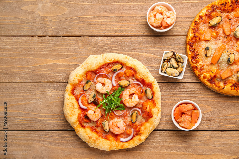 Tasty seafood pizzas and ingredients on wooden background