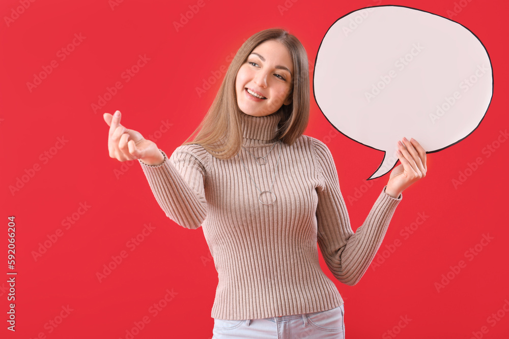 Young woman with blank speech bubble making heart shape on red background