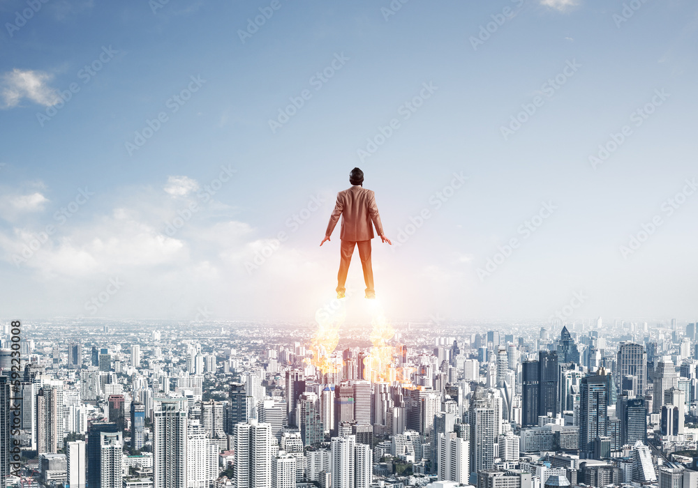 Businessman in suit and aviator hat flying in sky