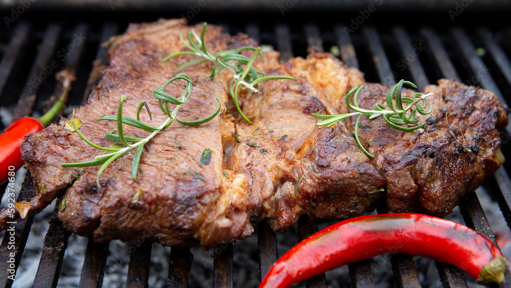 Beef steaks cooking on the charcoal grill with chili pepper, tomatoes, garlic and mushrooms for bbq 