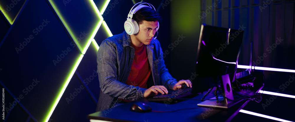 Young man playing an online video game on a pc, with a headset for communication with other gamers