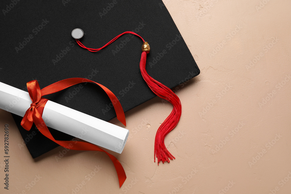 Diploma with red ribbon and graduation hat on beige table