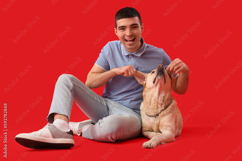 Young man with cute Labrador dog sitting on red background