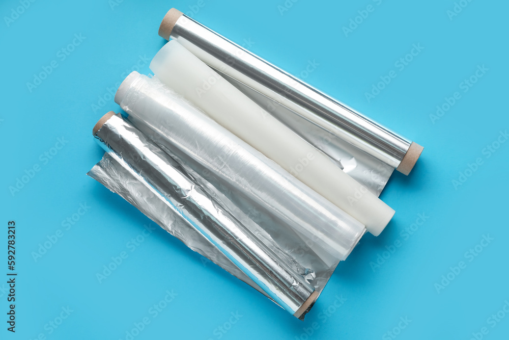 Rolls of aluminium foil, food film and baking paper on color background