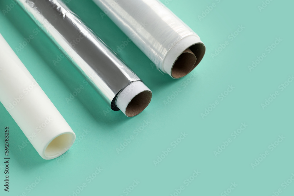 Rolls of baking paper, aluminium foil and food film on color background, closeup