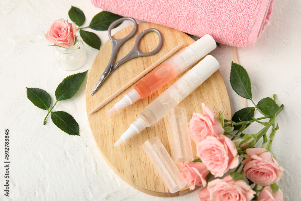 Composition with cuticle oil pens, manicure instruments and rose flowers on light background