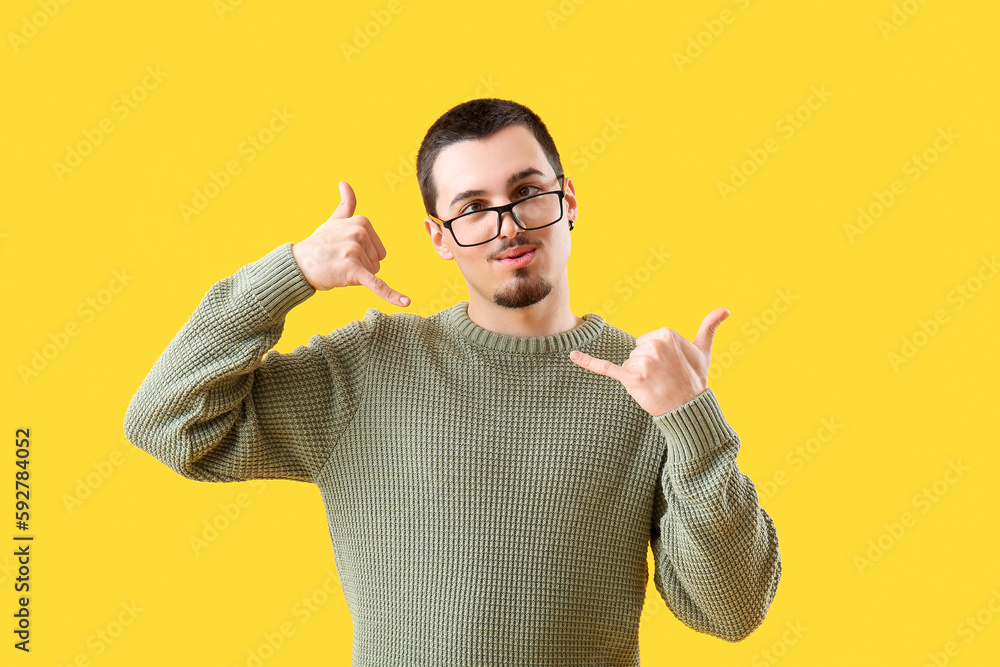 Funny young man showing  call me  gesture on yellow background