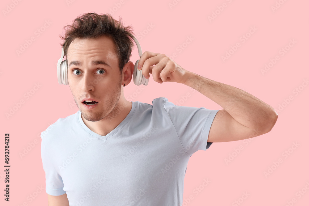 Shocked young man with headphones on pink background