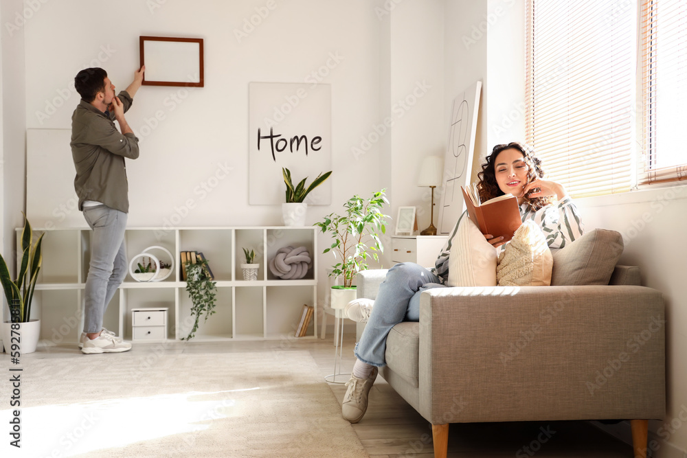 Young couple hanging blank frame on light wall at home