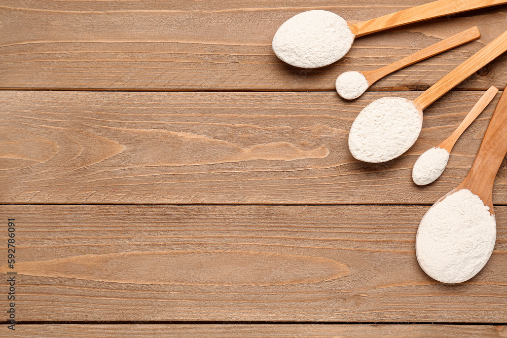 Wooden spoons with wheat flour on wooden table