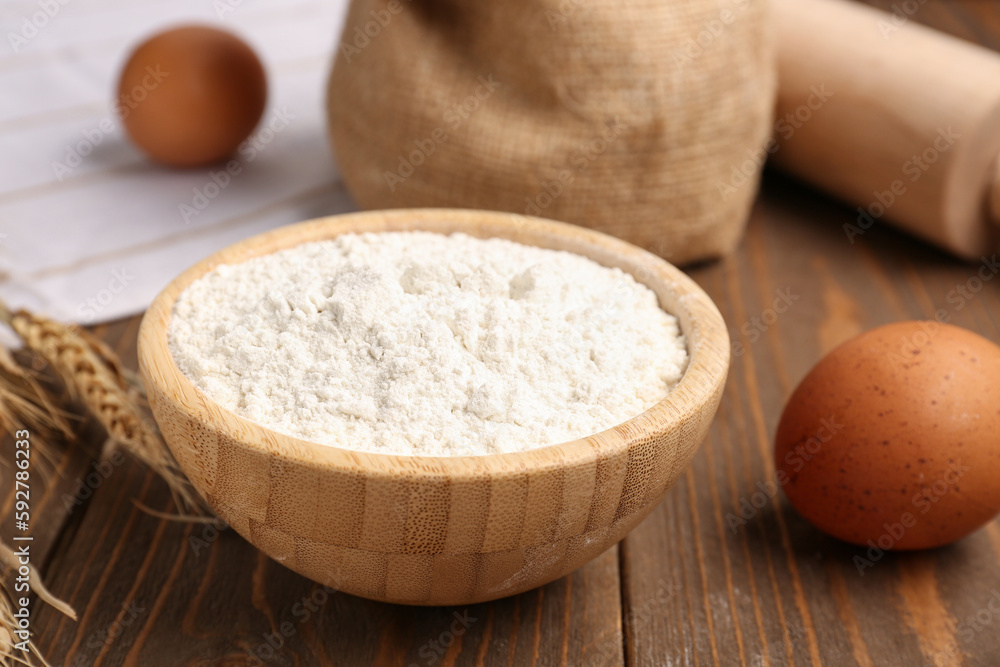 Bowl with wheat flour on wooden table, closeup