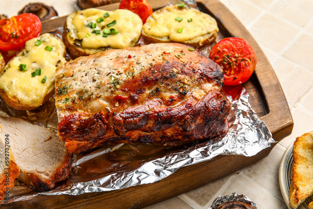 Wooden board with tasty baked meat, potatoes and tomatoes on table, closeup