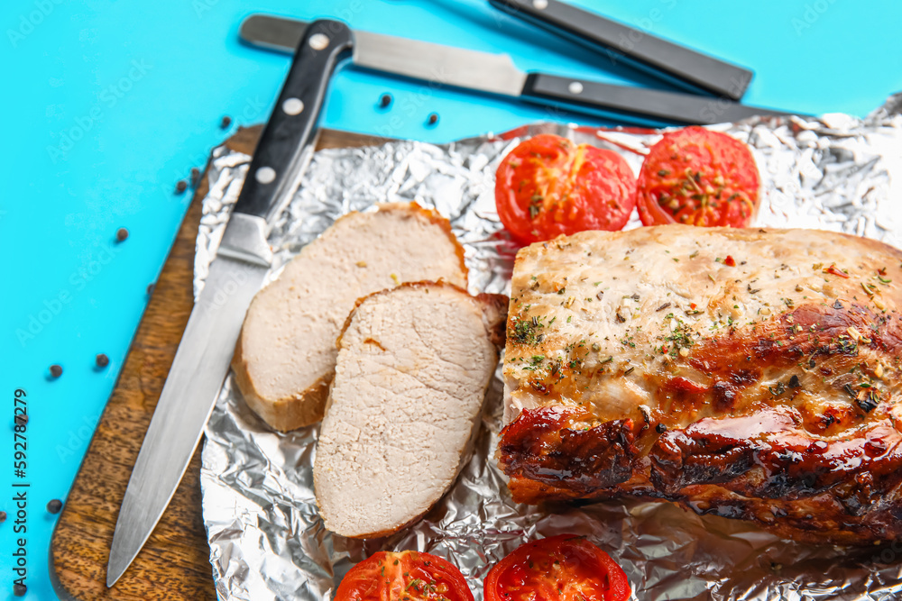 Wooden board with tasty baked meat, tomatoes, spices and cutlery on color background, closeup