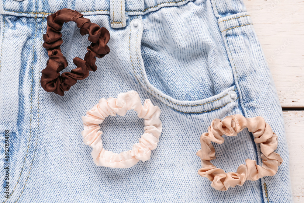 Silk scrunchies with jeans on white wooden background, closeup