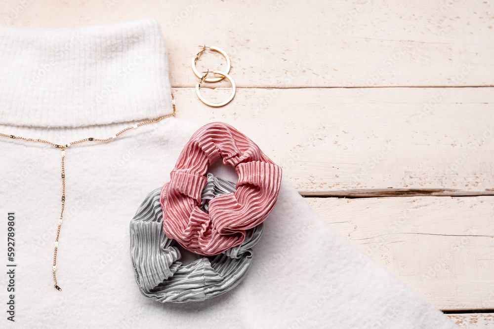 Silk scrunchies with jewelry and sweater on white wooden background, closeup