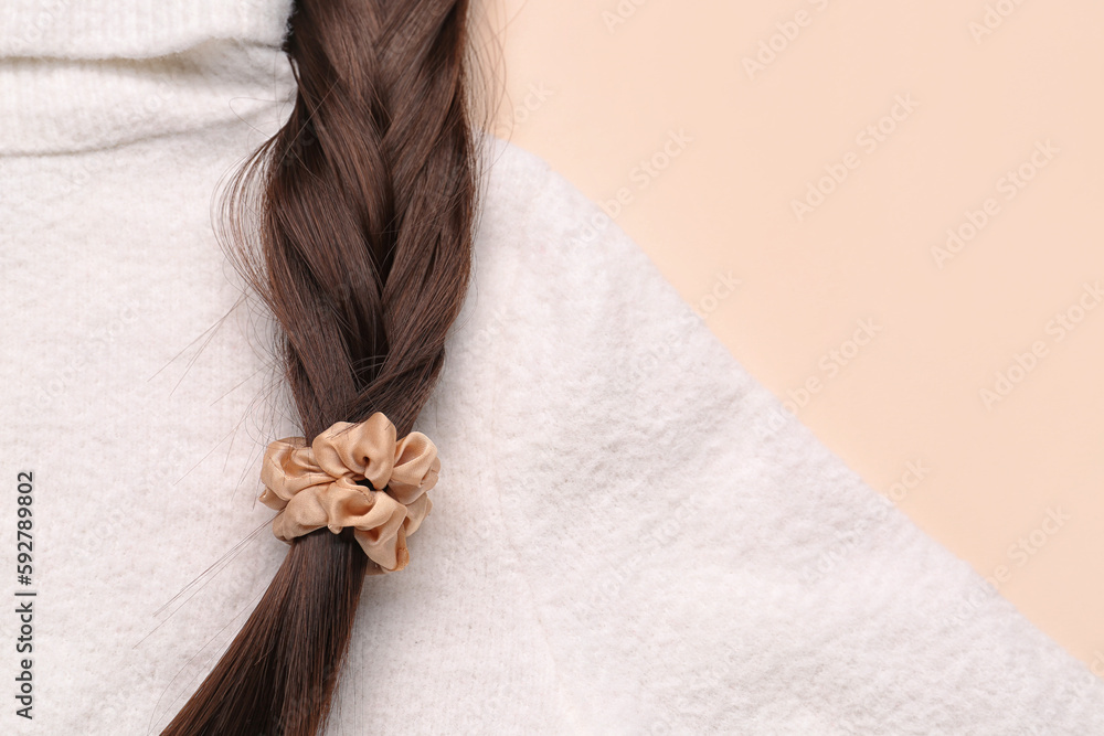 Braided hair strand with scrunchy and sweater on beige background, closeup