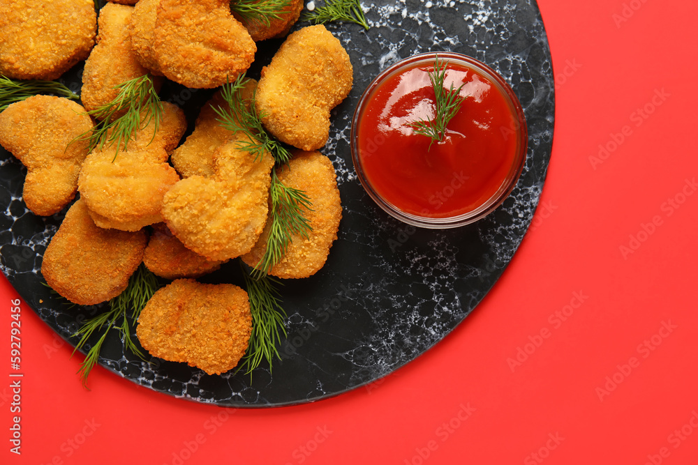 Slate board of tasty nuggets with ketchup on red background, closeup