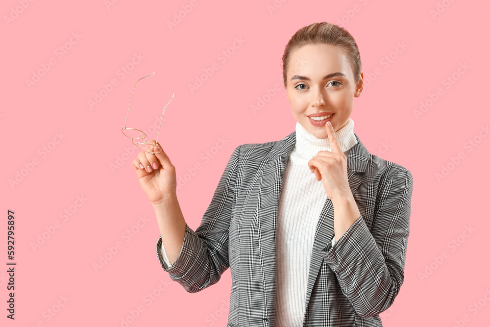 Thoughtful young businesswoman with eyeglasses on pink background