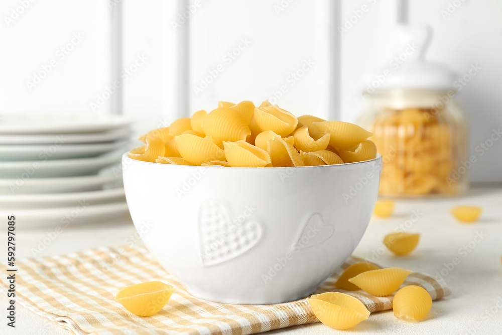 Bowl with raw conchiglie pasta on light background