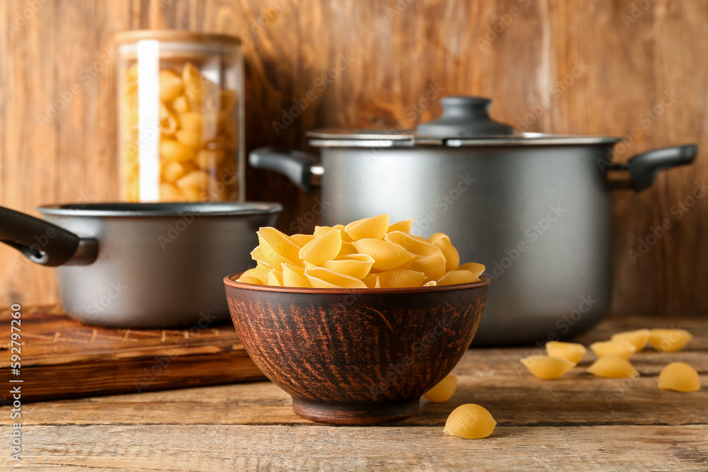 Bowl with raw conchiglie pasta on wooden background