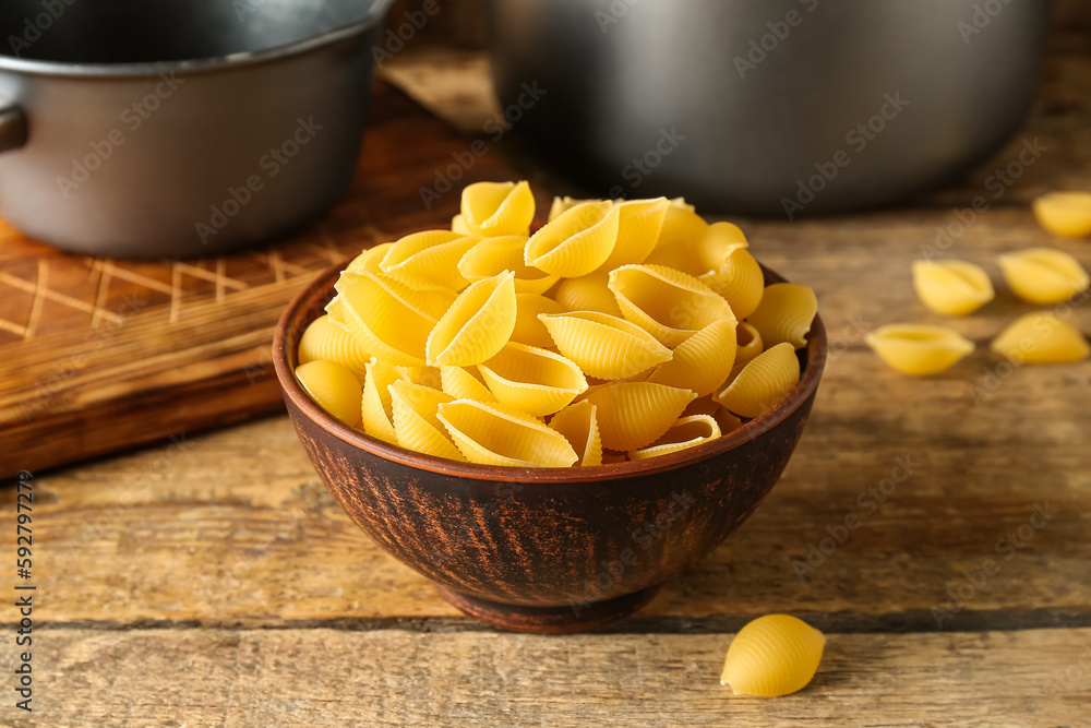 Bowl with raw conchiglie pasta on wooden background