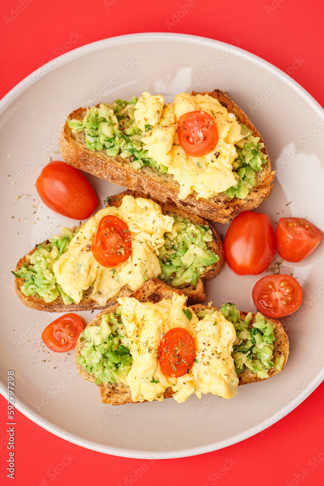 Plate with tasty scrambled eggs sandwiches and vegetables on red background