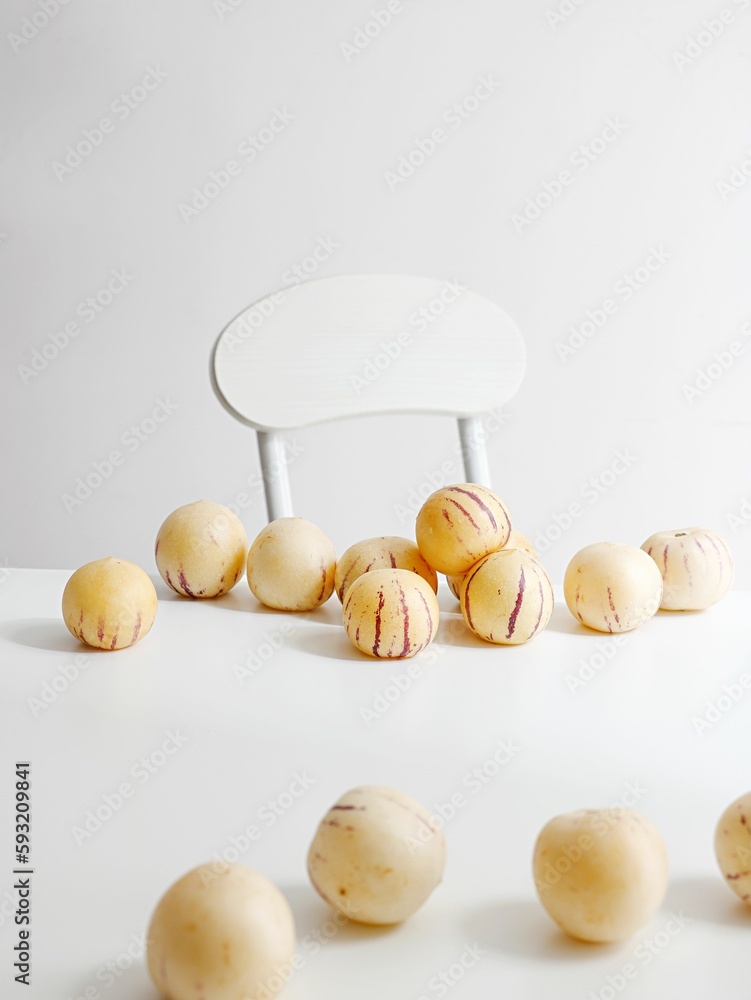 Vertical shot of fresh pepino melons on white table with a chair in background