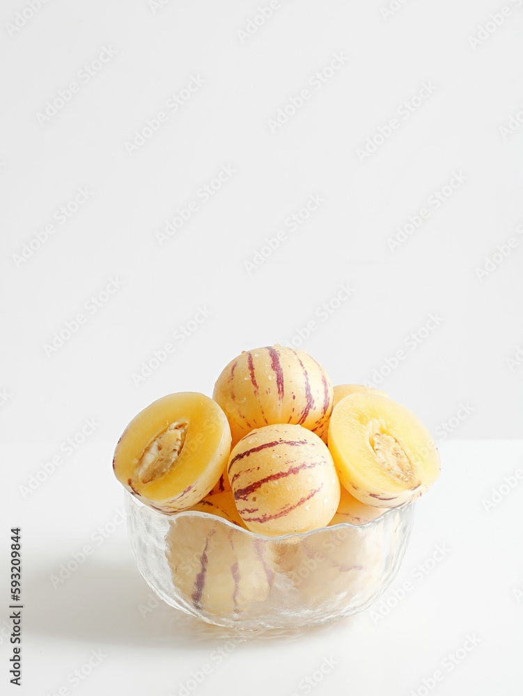 Vertical shot of fresh pepino melons in glass bowl on white table