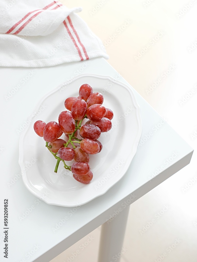 Vertical shot of red grape in a white plate with a kitchen towel on a table