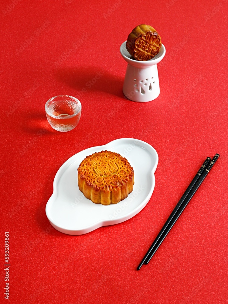 Vertical shot of mooncakes in white plates, a glass of tea and chopsticks on red background