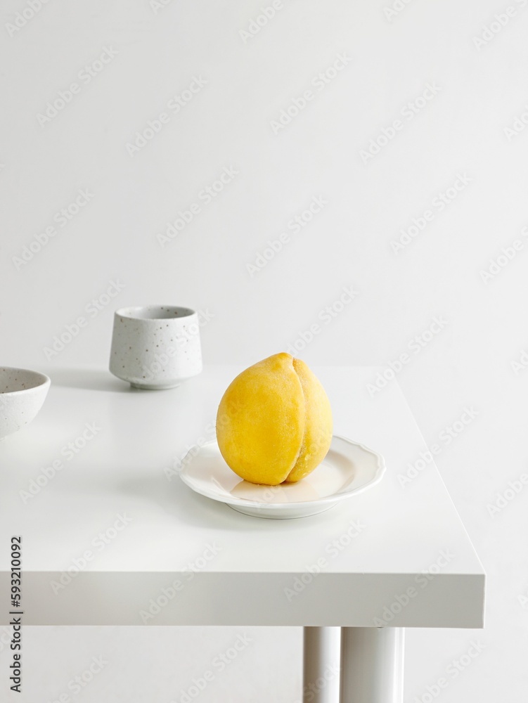 Closeup of a yellow peach on a white plate in a minimalistic decor background