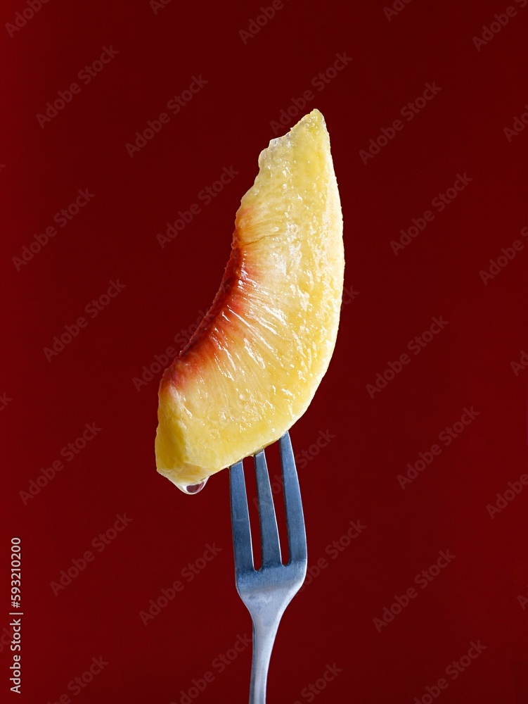 Closeup of a peach slice on a fork in a maroon background