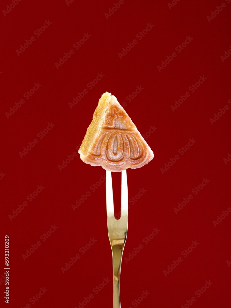 Closeup of a tiny cookie slice with a floral ornament stamp on a maroon background