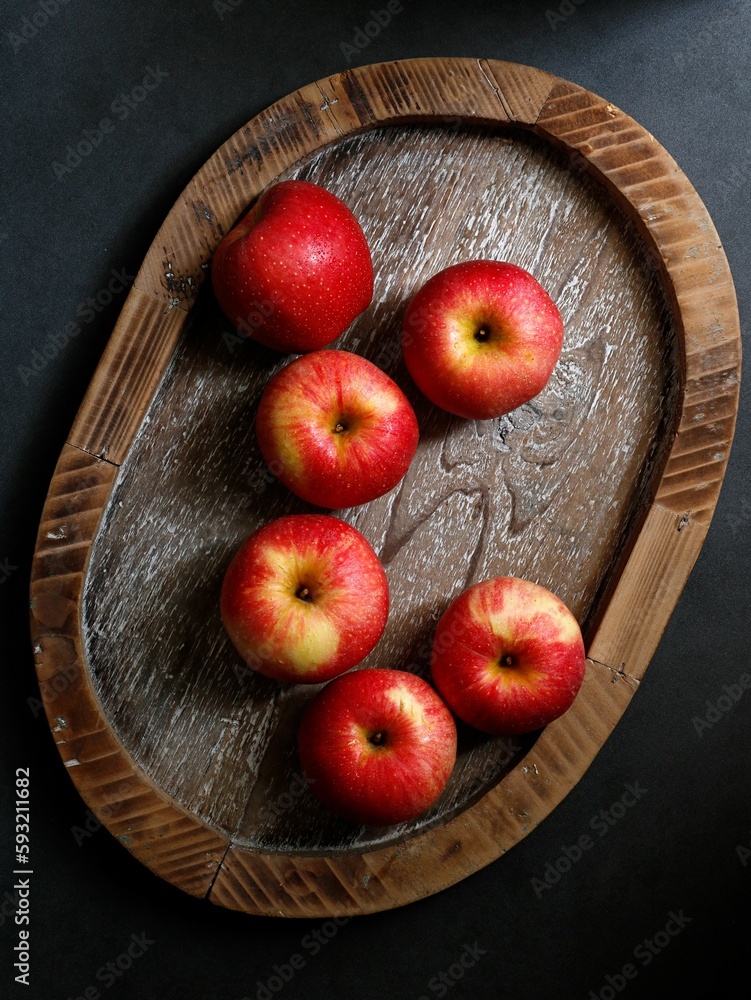 Vertical shot of red apples on a wooden tray on a black table