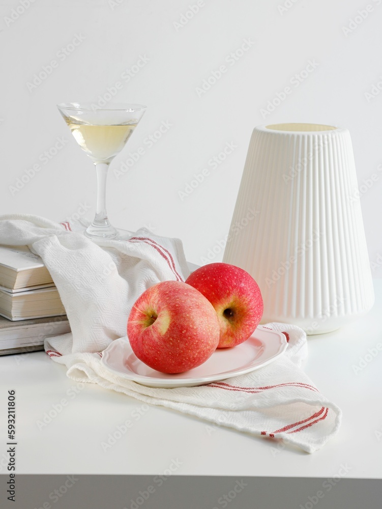 Vertical shot of a plate of red apples, a vase, a kitchen towel and a martini glass on white table