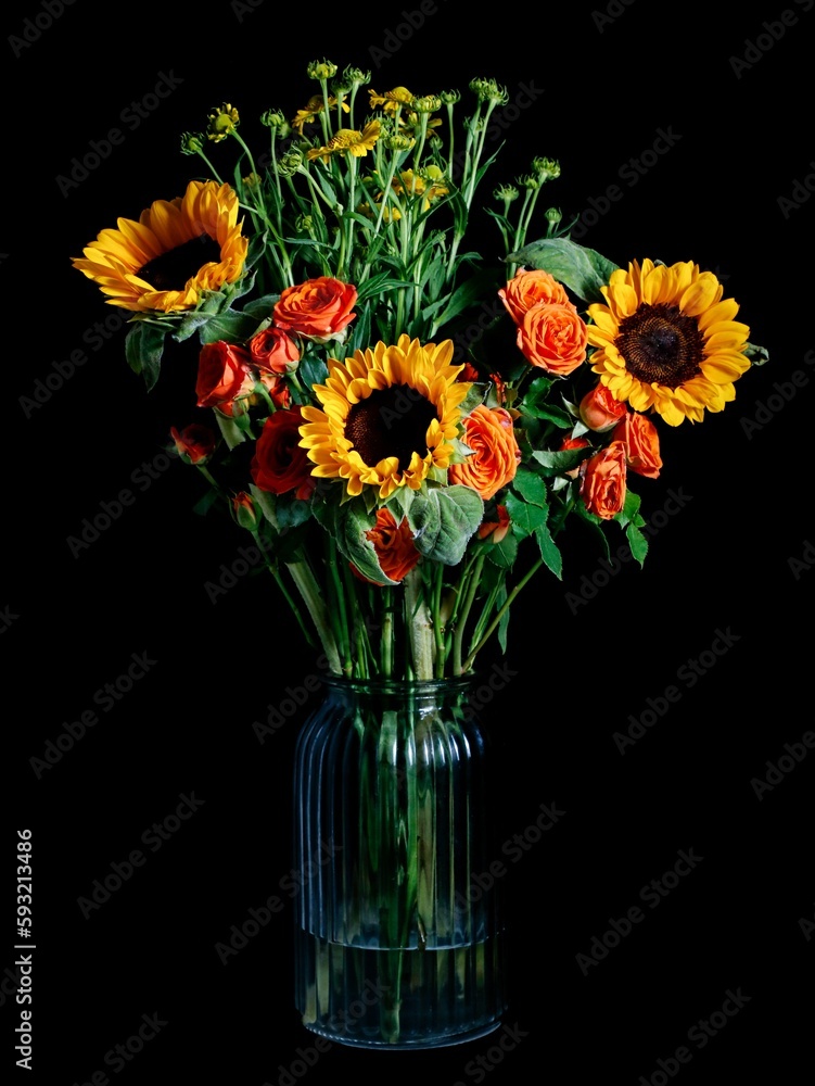 Vertical shot of a bouquet of sunflowers and roses in a vase isolated on a dark background