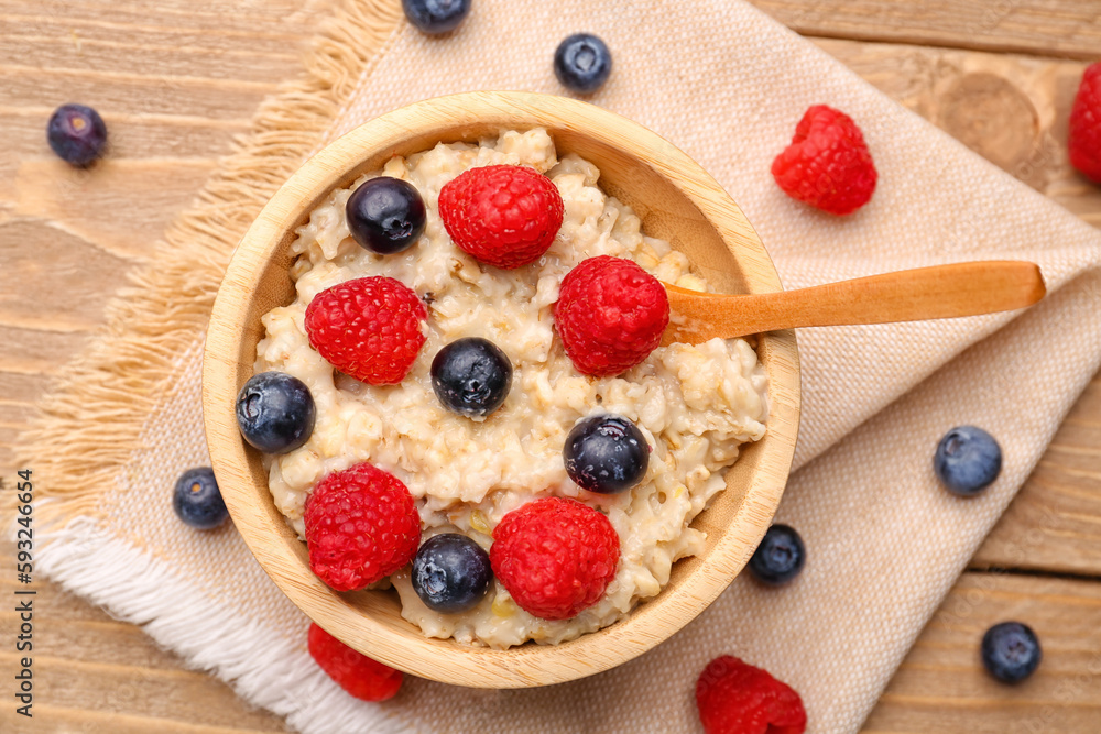 Bowl with tasty oatmeal, blueberries and raspberries on wooden background