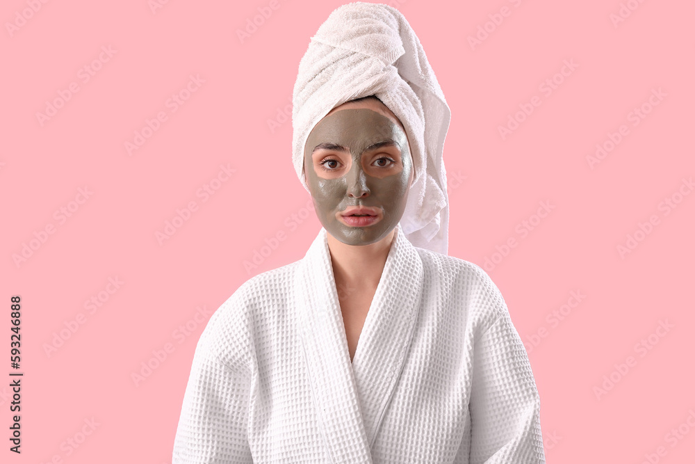 Young woman in bathrobe with applied clay mask on pink background