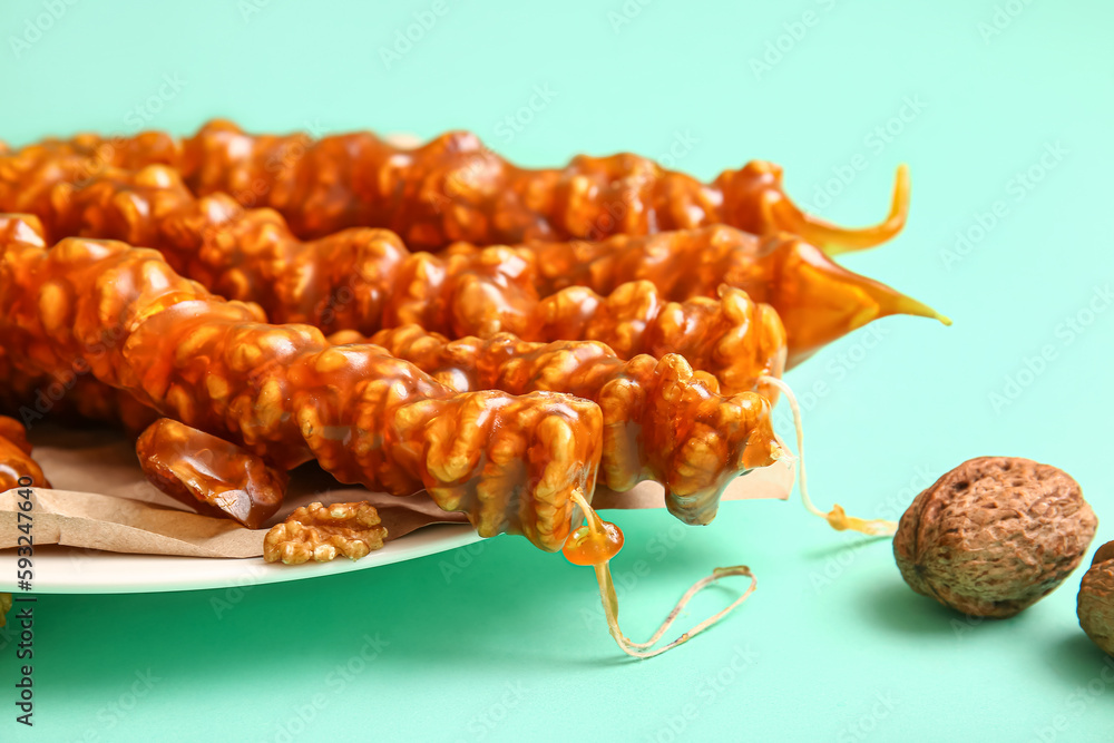 Plate with tasty churchkhela and walnuts on color background, closeup