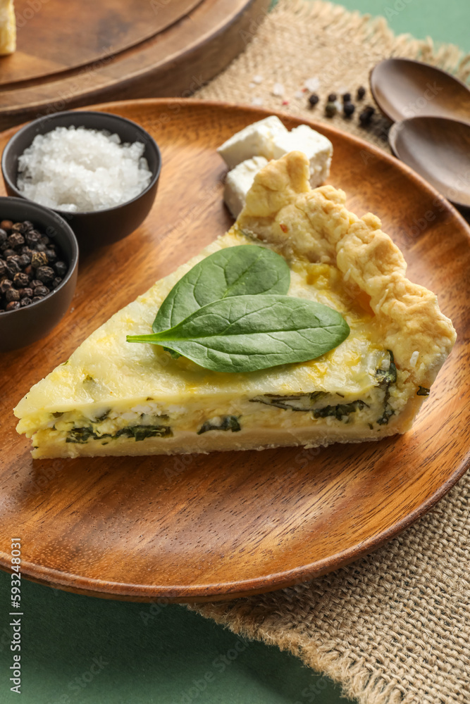 Plate with piece of delicious quiche and spices on green background