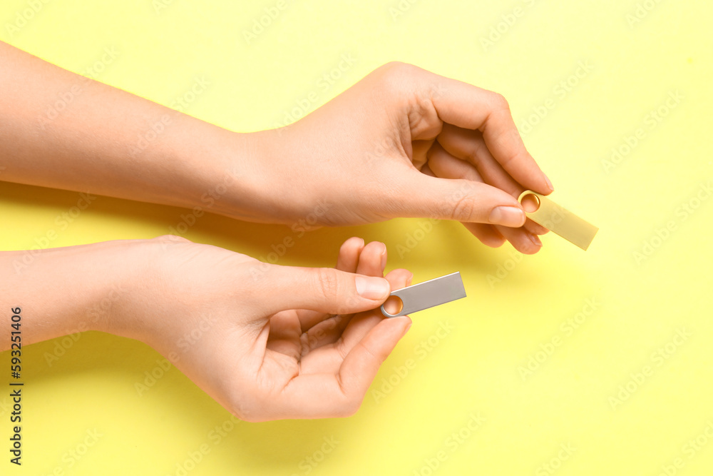 Female hands holding metallic and golden USB flash drives on yellow background