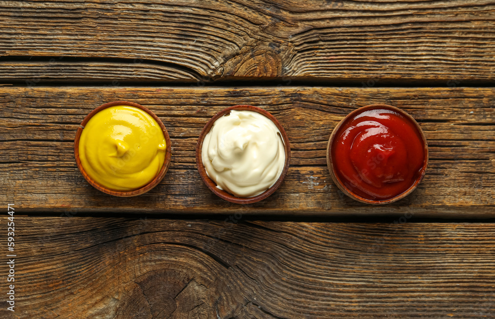 Bowls of ketchup, mayonnaise and mustard on wooden table