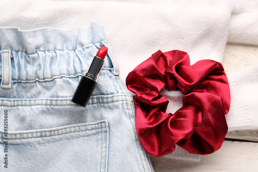 Silk scrunchy with lipstick and jeans on white wooden background, closeup