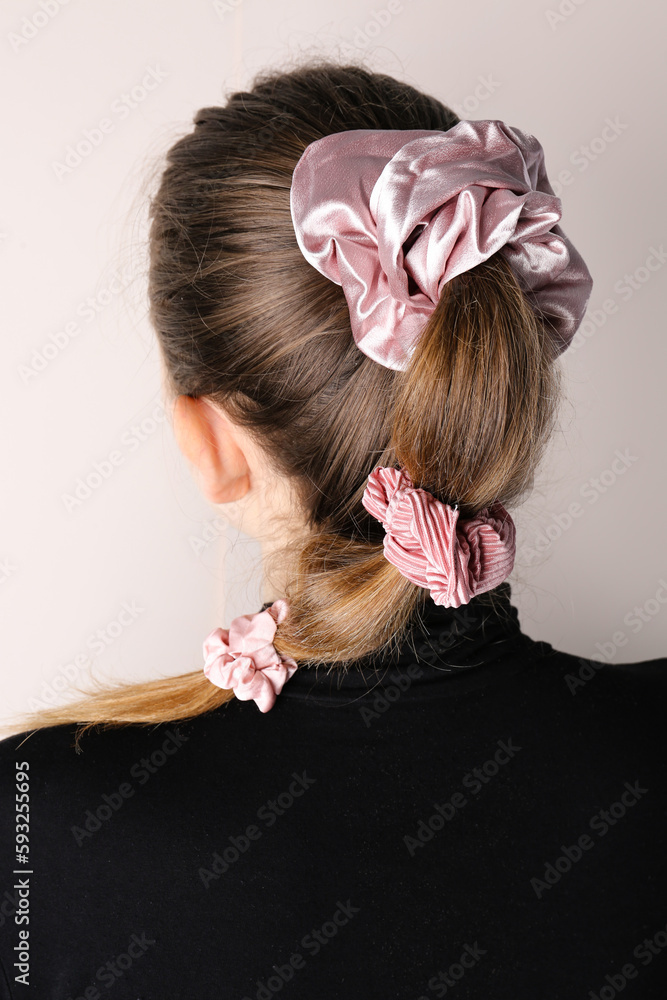 Woman with stylish hairdo and silk scrunchies on light background, back view