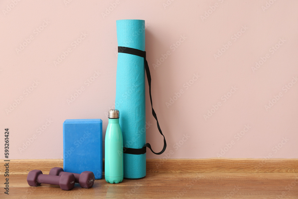 Dumbbells with fitness mat, block and bottle near pink wall