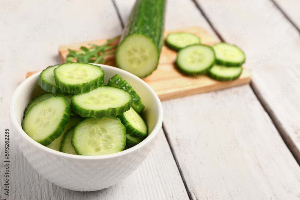 Bowl with fresh cut cucumber on light wooden background