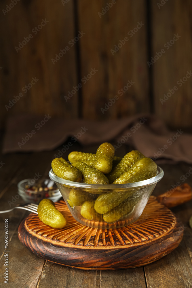 Bowl with tasty fermented cucumbers, board and ingredients on wooden table