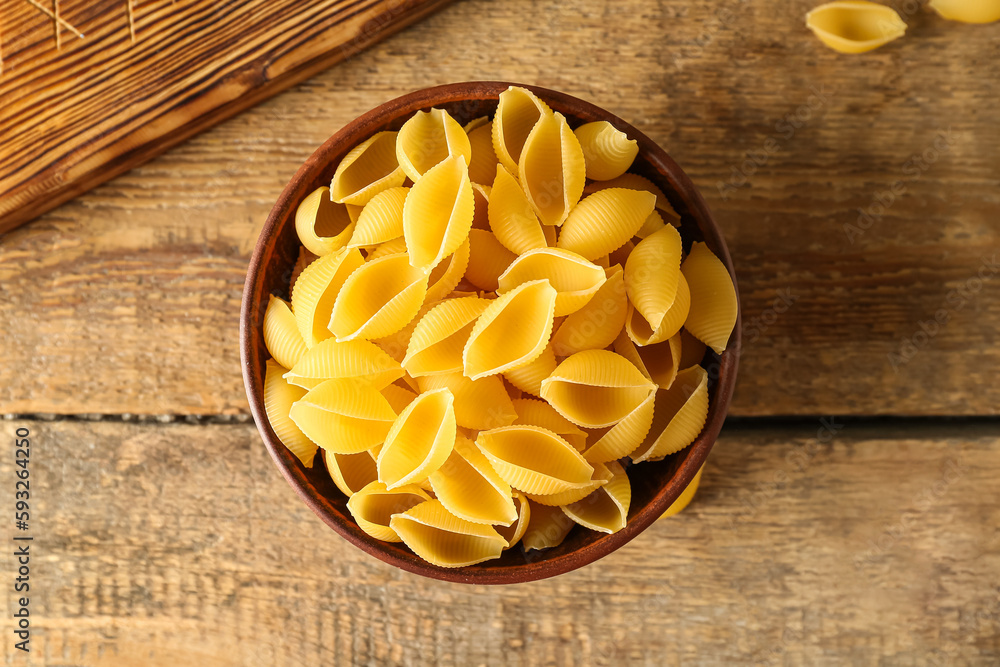 Bowl with raw conchiglie pasta on wooden background