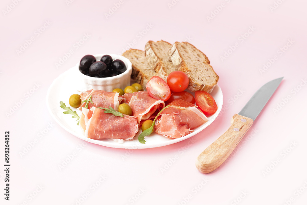 Plate with slices of tasty jamon with bread on pink background