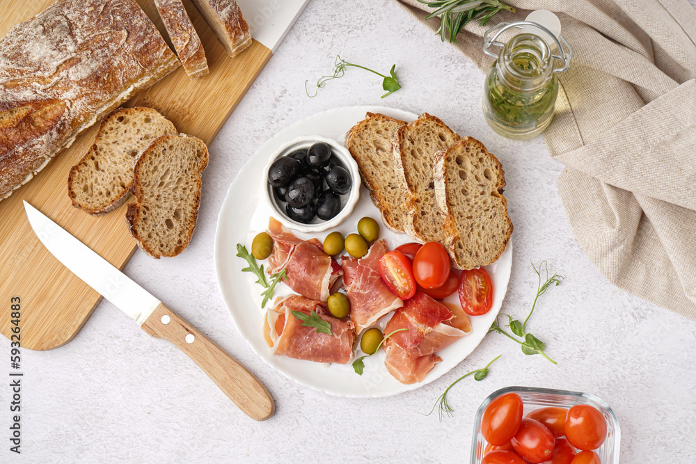 Plate with slices of tasty jamon and bread on light background